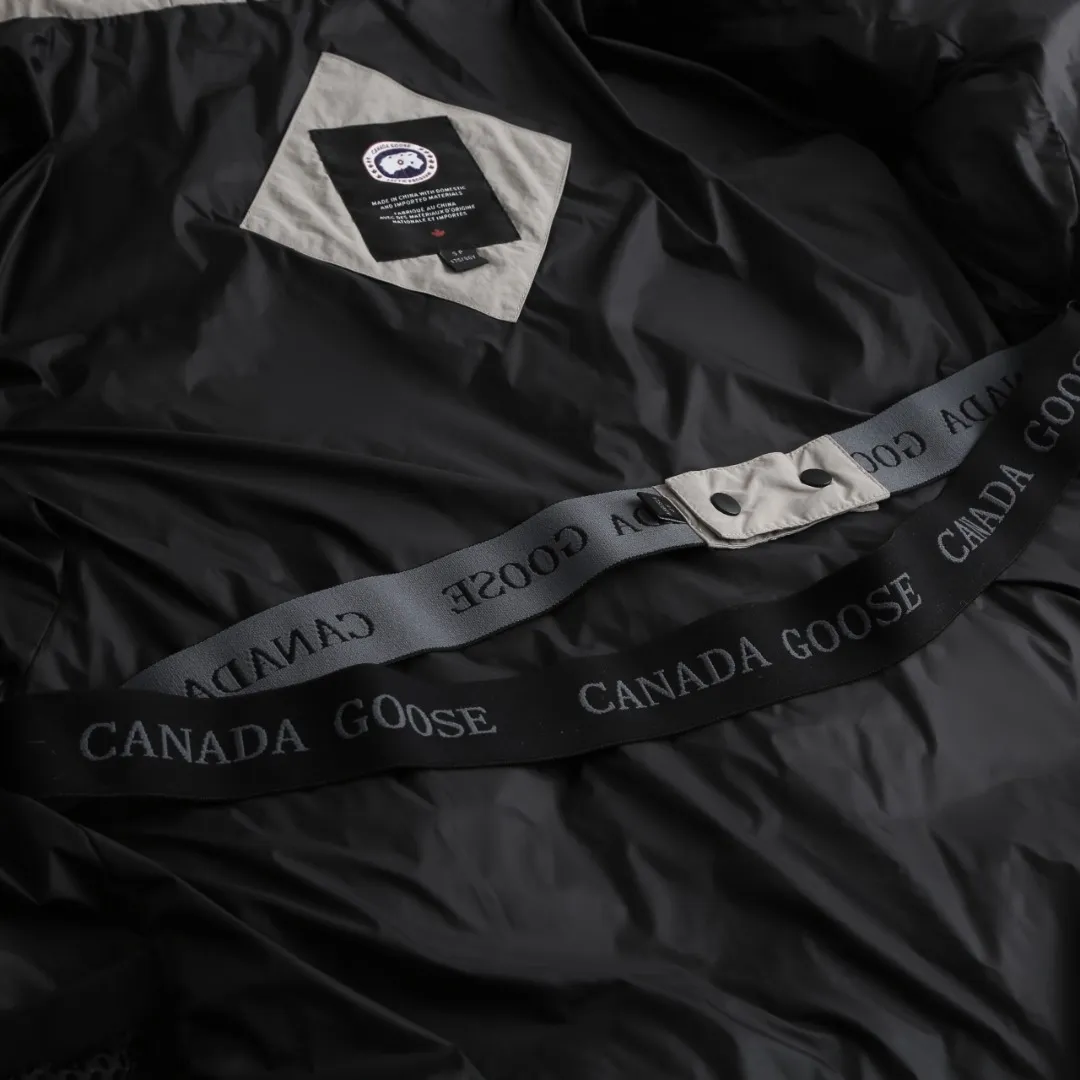 P980 Canada Goose hooded down jacket Fabric selection: Weaved with 400T high-count yarn. After special water-repellent treatment, the surface forms a lotus leaf effect - raindrops will slide down in beads, and snow particles will fall off when touched. The tear resistance reaches 200N (approximately 20kg load-bearing), the light gray matte texture breaks the stereotype of "outdoor clothing = hardcore", and the soft luster presents a high-end matte effect under urban neon lights, seamlessly switching scenes from ski resorts to CBD office buildings.  Process 1: Use polyester woven ribbons as the base, and use high-precision computer embroidery to decorate the brand letters on the ribbons. The edges of the pattern are clear, the stitches are fine and even, and multiple layers of embroidery threads are stacked to enhance the three-dimensional effect.  Process 2: Precision thread reinforcement to prevent velvet drilling and ensure that the fluffy and resilient elasticity lasts as new.  Details: The embedded cuffs are three-dimensionally woven to form a "wavy" elastic structure, forming natural folds when fitting the wrist, increasing the contact area with the skin, thus improving the windproof effect. At the same time, micro-velvet treatment is added to the inside of the cuffs, which feels like a second layer of skin and avoids friction on the skin from metal zippers or hard fabrics.  90 national standard high-quality white duck down: selected high-loft down, weighing 240g, light and warm, with excellent temperature locking performance and good resilience.  Accessories: 1:1 customized armband, 1:1 customized zipper pendant, 1:1 customized elastic buckle, etc. SIZE: S M L XL